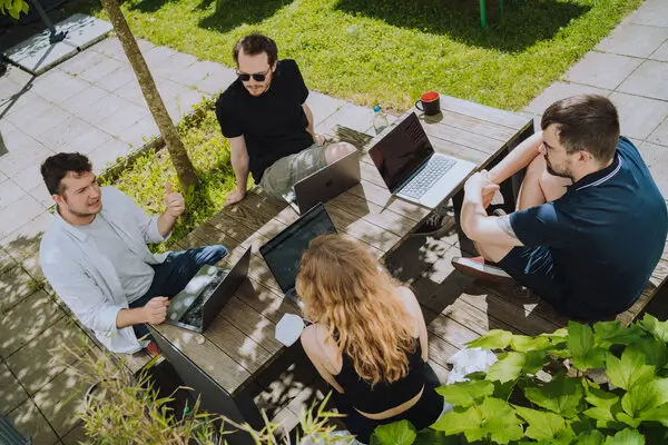 Drei Kollegen und eine Kollegin halten ein Meeting an einem Gartentisch.
